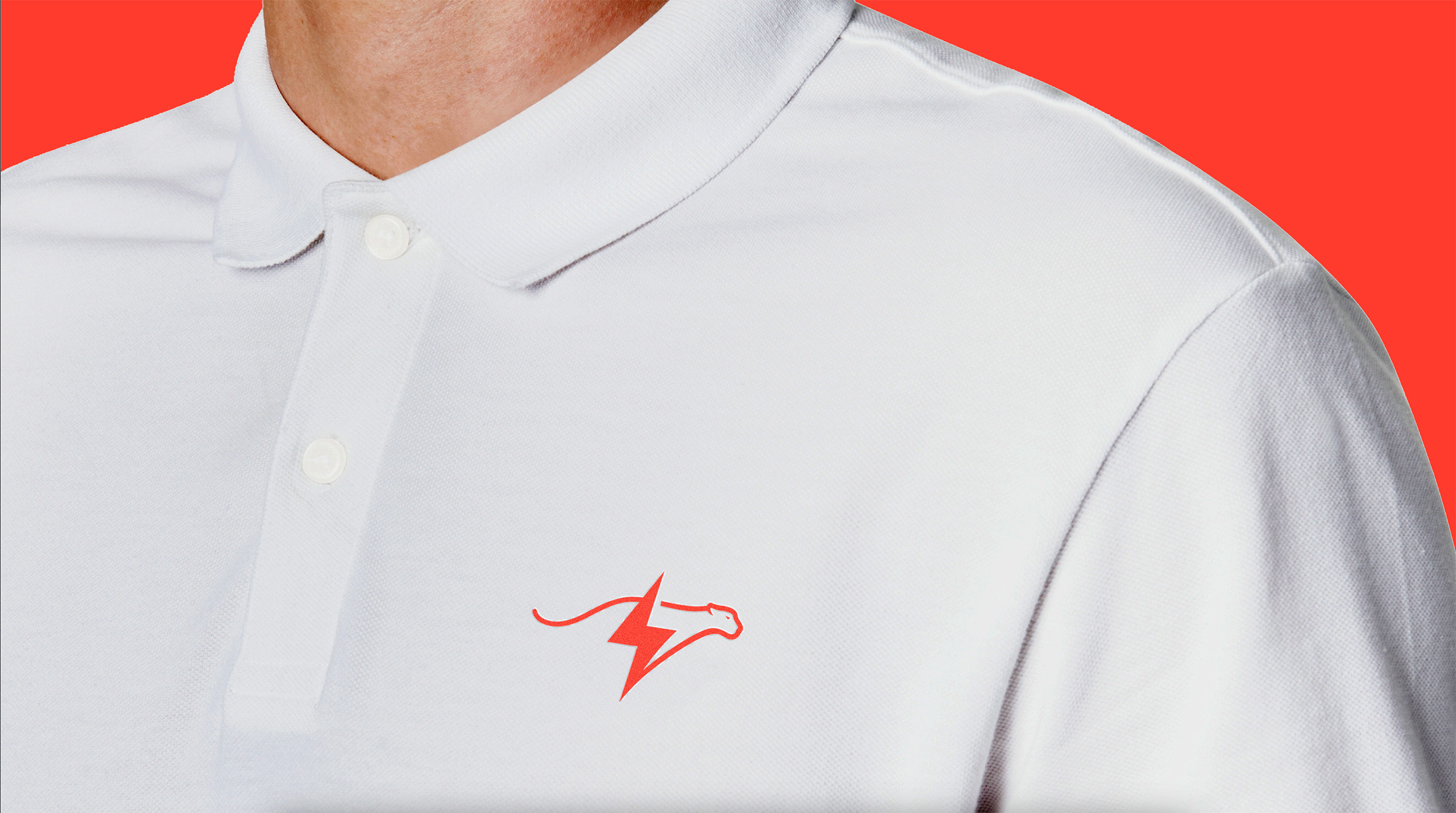 Close-up van een wit poloshirt met een rood bliksembout-logo, tegen een rode achtergrond