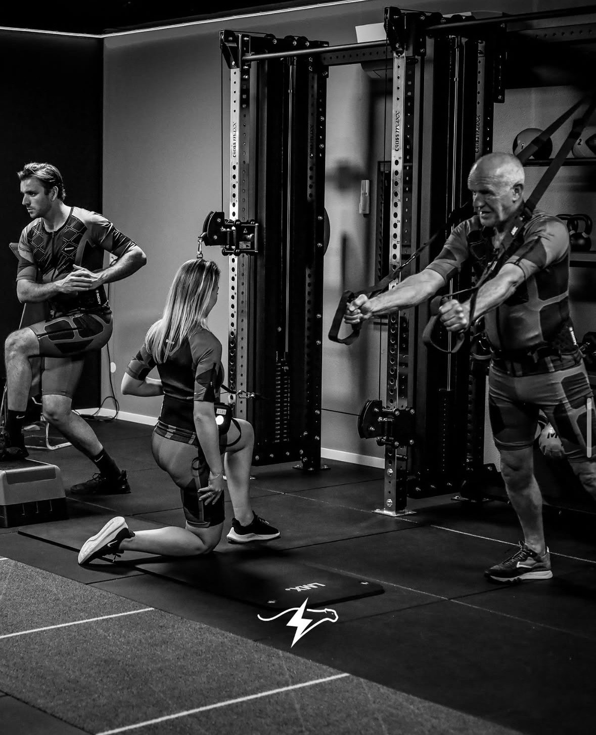 Personal trainer begeleidt een oudere man en een vrouw bij een work-out in de sportschool