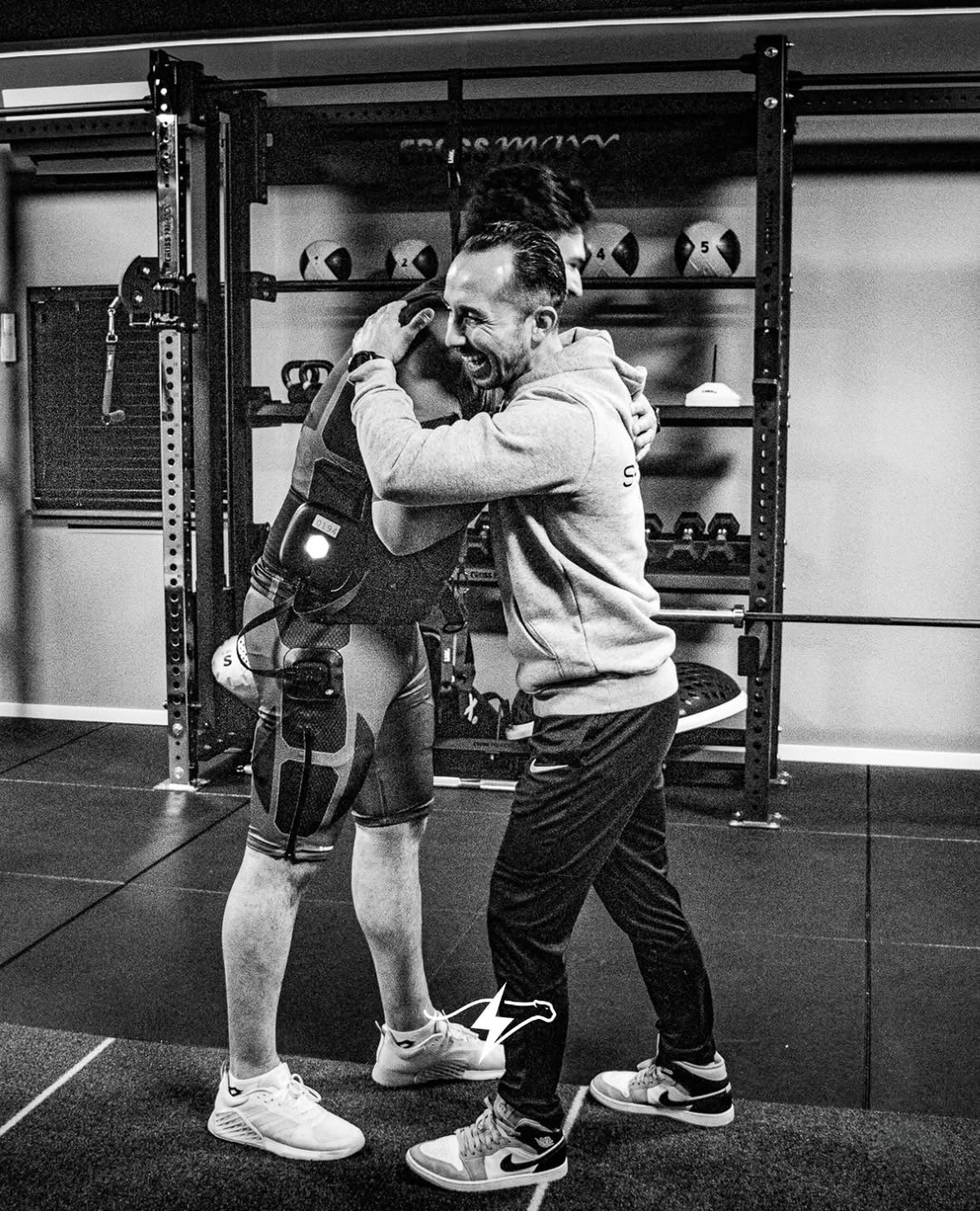 Twee mannen lachen en omhelzen elkaar in een sportschool, één met een bokspad