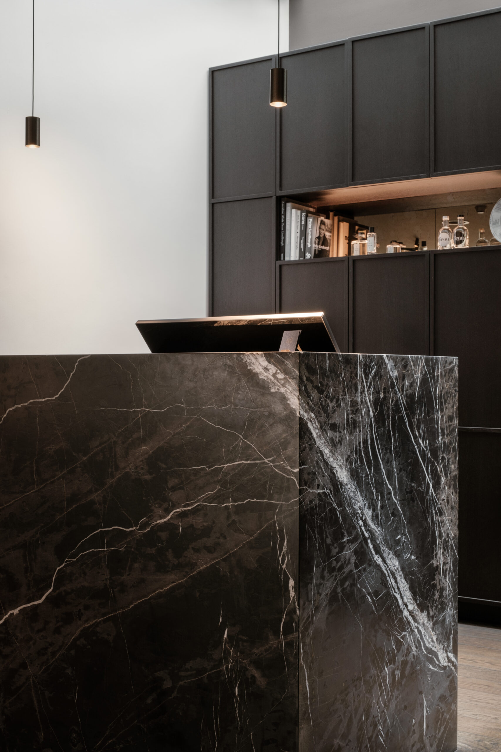 Detail van een marmeren balie met sterke adering, hanglampen en een kast met glaswerk op de achtergrond