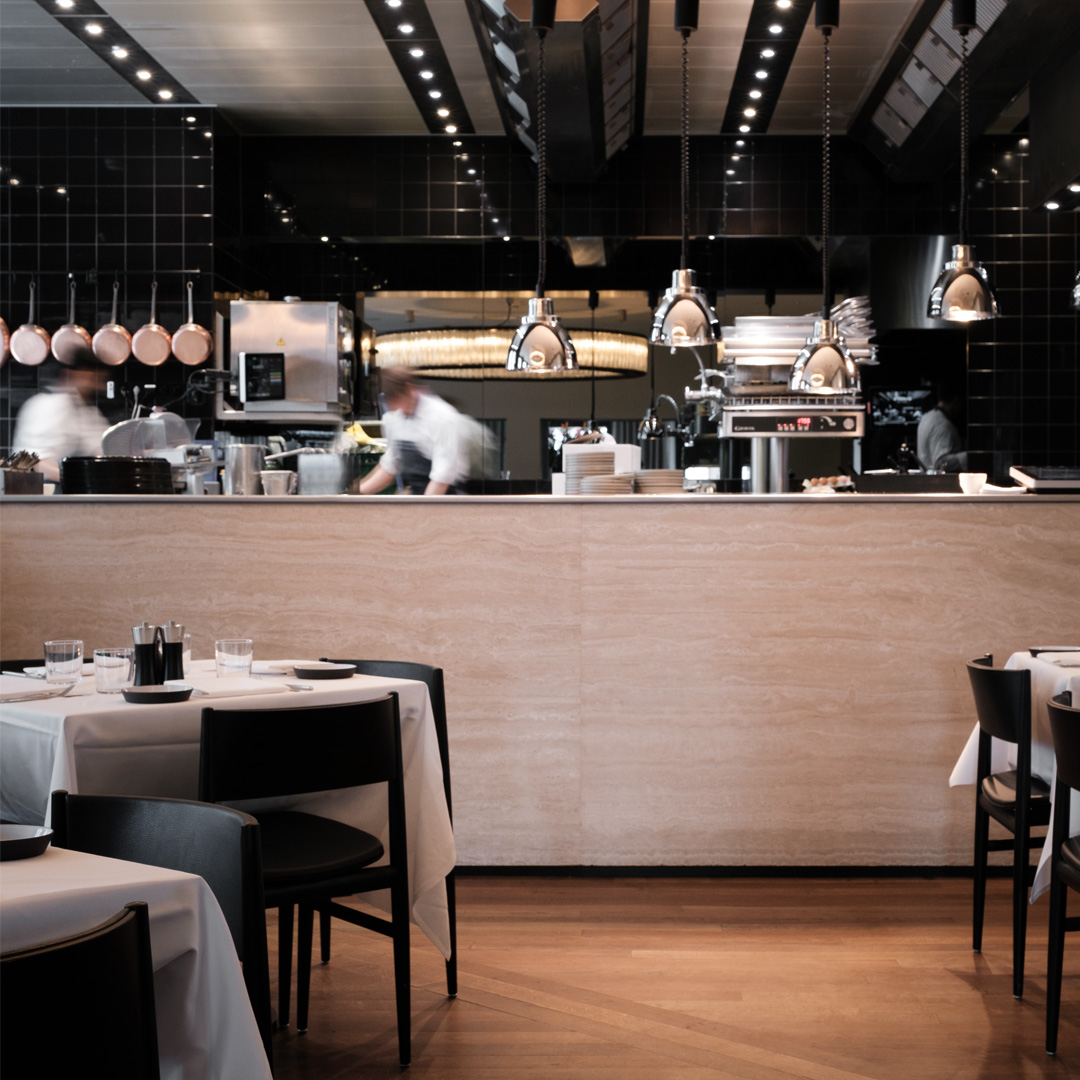 Restaurant met open keuken en koks aan het werk, koperen hanglampen boven eettafels en barkrukken