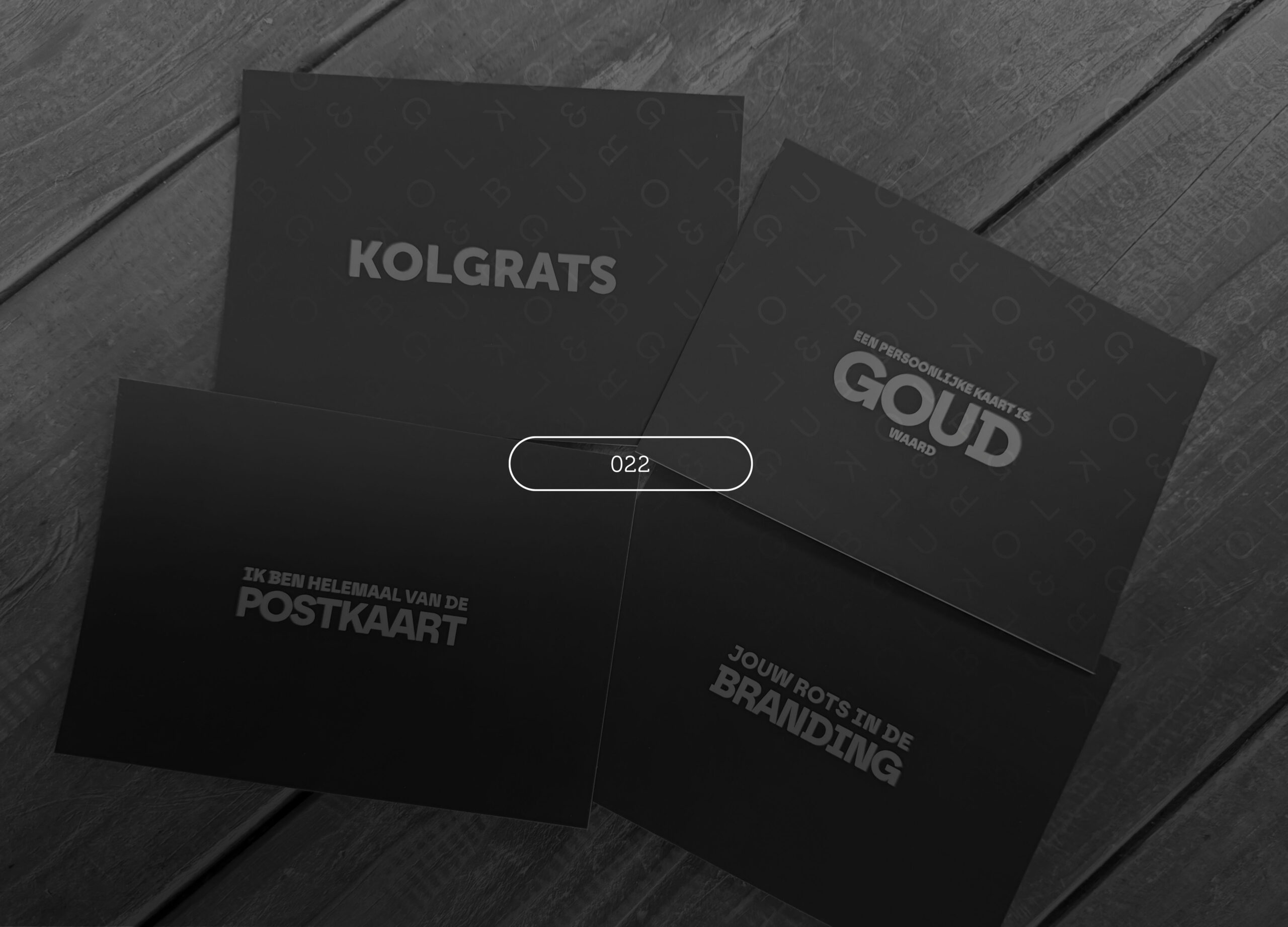 Four dark postcards reading Kolgrats, Goud, Postkaart and Branding on a wooden table