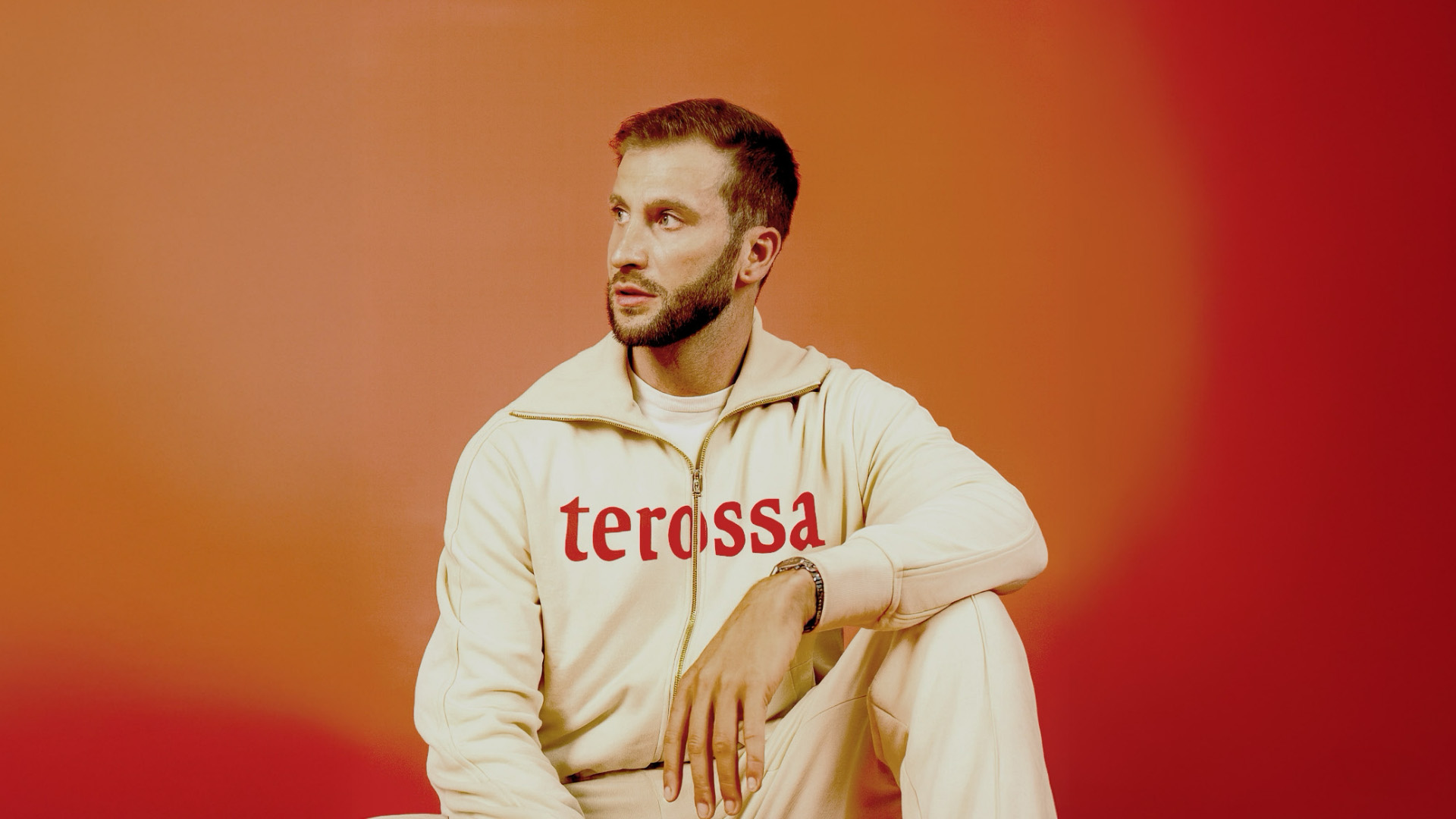 Man in een crèmekleurige hoodie met het woordmerk 'terossa', tegen een oranje achtergrond